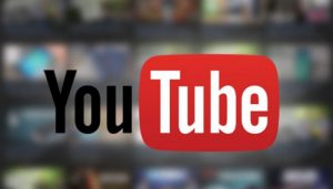 Logo di Youtube nero, rosso e bianco con sullo sfondo alcuni schermi di computer sfocati